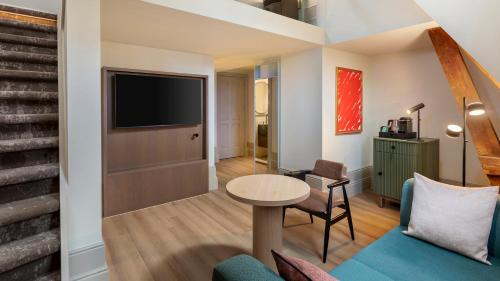 a living room with a couch and a table and a tv at The College Hotel Amsterdam, Autograph Collection in Amsterdam