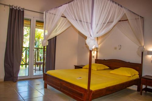 a bedroom with a canopy bed with yellow sheets at Résidence Kambana in Nosy Be
