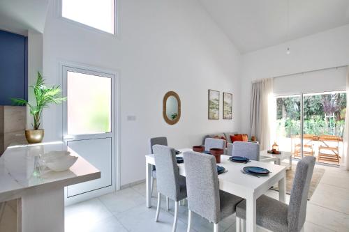 a white dining room with a white table and chairs at Aphrodite Gardens Modern Villas by VICHY Holidays in Paphos