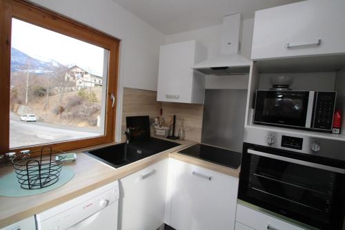 eine Küche mit einer Spüle, einer Mikrowelle und einem Fenster in der Unterkunft Apartment LA ROCHETTE free parking on site in Guillestre