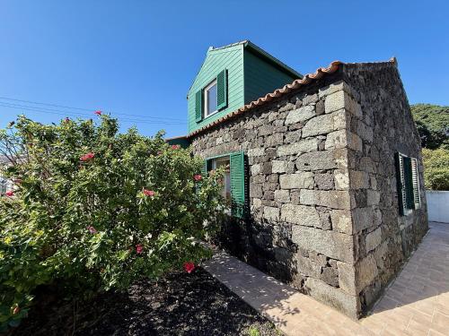 a brick house with a green window and a bush at Musa do Pico in Madalena
