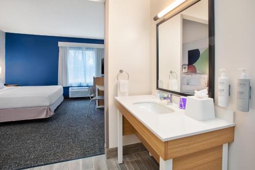 a bathroom with a sink and a bed and a mirror at Spark by Hilton Walker Grand Rapids North in Grand Rapids