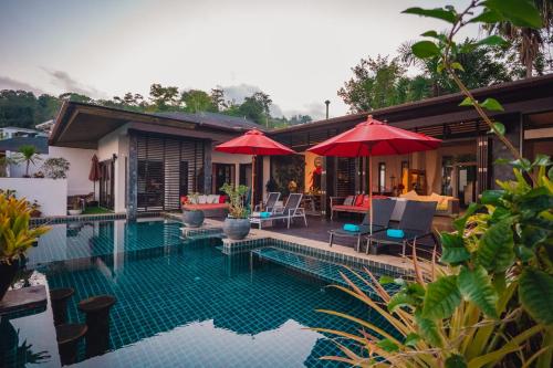 una casa con piscina con sillas y sombrillas en Chalong Sunset Villa, en Chalong 