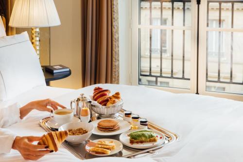a tray of breakfast foods on a bed at Maison Barrière Vendôme in Paris