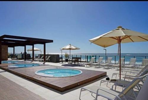 a swimming pool with chairs and umbrellas on a beach at Apartamento Pé na Areia Barra Velha in Barra Velha