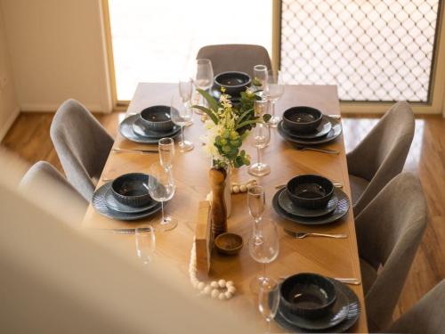 a wooden table with plates and wine glasses on it at Ocean View From Balcony 5BR Home with Pool at Redcliffe in Clontarf