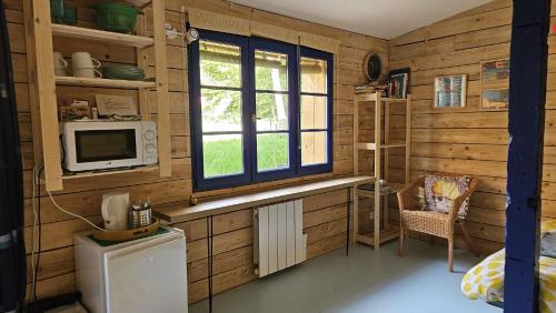 a kitchen with wooden walls and a microwave and a window at La cabane, Chambre indépendante dans jardin - Esprit cabane authentique et confortable - la campagne à 5 mn du centre de Caen in Fleury-sur-Orne