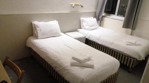 two beds in a room with white sheets and pillows at The Brentwood Hotel Porthcawl in Porthcawl