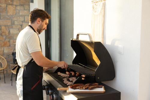 a man is cooking food on a grill at Flamingo Living Halkidiki - The Villas in Áyios Mámas