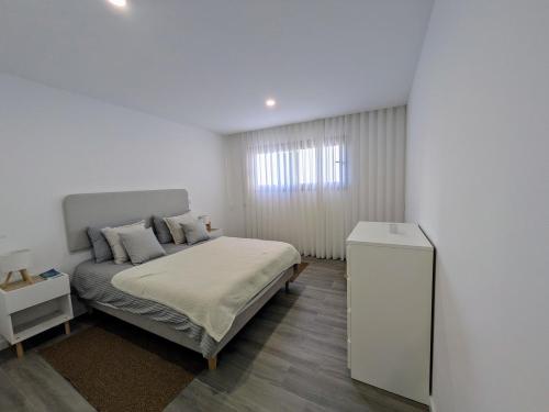 a white bedroom with a bed and a window at Porta da Praia - Paredes da Vitória in Senhora da Vitória