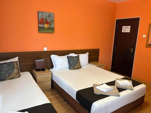 two beds in a room with orange walls at Family Hotel Flora in Zlatograd