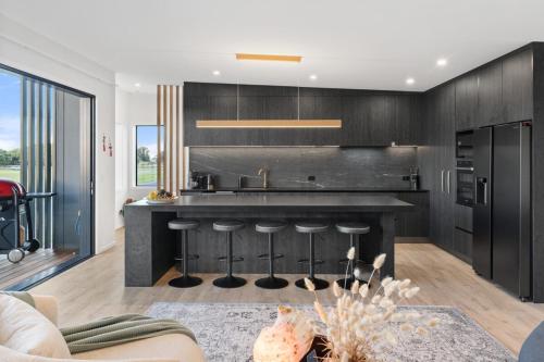 a kitchen with black cabinets and a kitchen island at Luxury Papamoa Beach House with Pool and Spa Pet Friendly in Papamoa