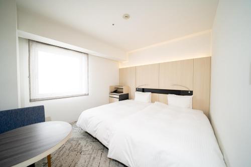 a bedroom with a white bed and a table at Hotel Sunroute Tokushima in Tokushima