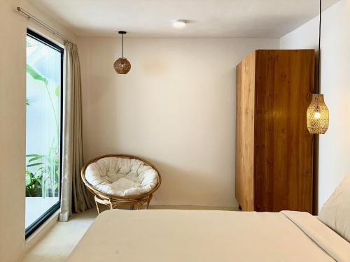 a bedroom with a bed and a chair and a window at The Ulu Hills in Uluwatu