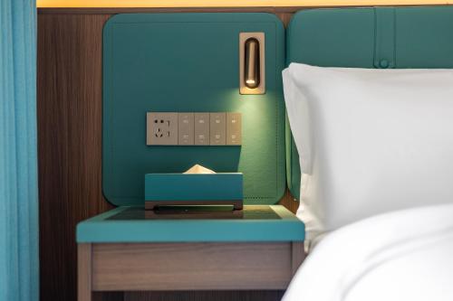 a bed with a blue suitcase on a table next to a bed at Merrihod Hotel - Guangzhou South Station Jinlong Subway Station Branch in Shunde