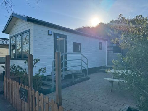 a white tiny house with a porch and a bench at Chalet Duinpan in IJmuiden