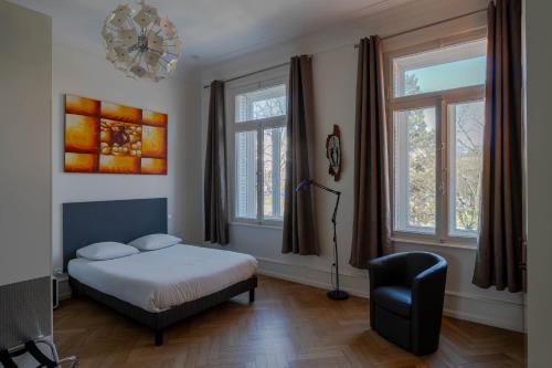 a bedroom with a bed and a chair and windows at Le Relais de l'Orangerie in Strasbourg