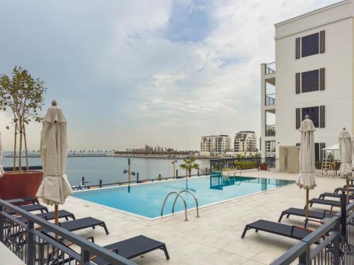 a pool with chairs and umbrellas next to a building at High-End Luxury 1BR in Port De La Mer near J1 Beachfront, Dubai in Dubai