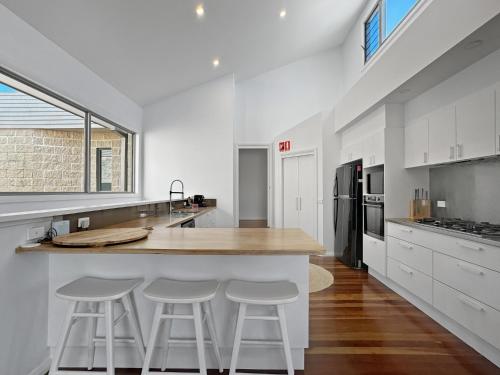 a kitchen with white cabinets and a counter with stools at Serene Luxury Retreat on Malua Bay in Malua Bay