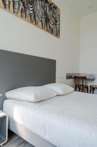 a bed with white sheets and a picture on the wall at La Résidence de l'Orangerie in Strasbourg