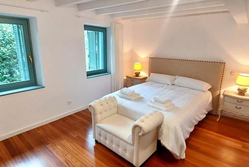 a bedroom with a white bed with a chair and two windows at MoM Comillas in Comillas