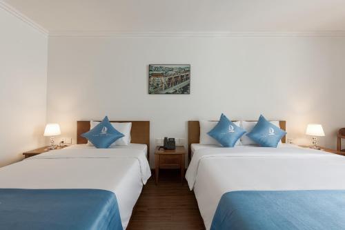 two beds in a hotel room with blue pillows at Hanoi Sail Hotel in Hanoi