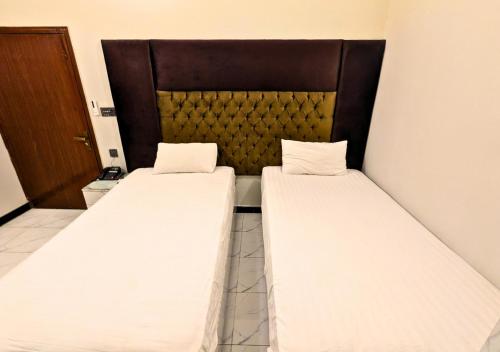 two beds in a hotel room with white sheets at Dove Inn Hotel wahdat road in Lahore