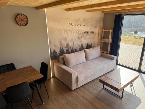 a living room with a couch and a table and a clock at Domki Nad Stawami z Jacuzzi i Sauną 4 in Wolibórz