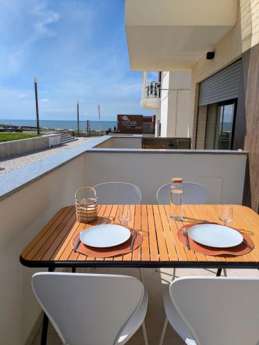 a wooden table with two plates on a balcony with chairs at Porta da Praia - Paredes da Vitória in Senhora da Vitória