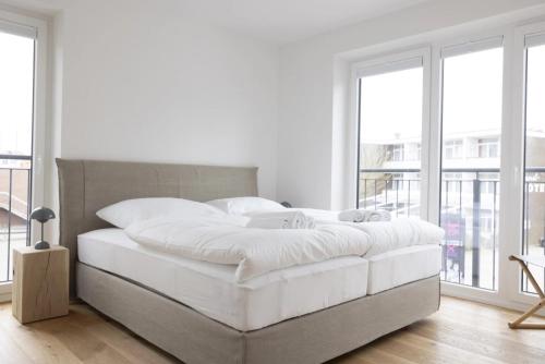 a white bedroom with a large bed and windows at Mole in Sankt Peter-Ording