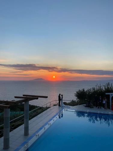 a bride and groom standing next to a swimming pool with the sunset at Villa Solaria in Massa Lubrense