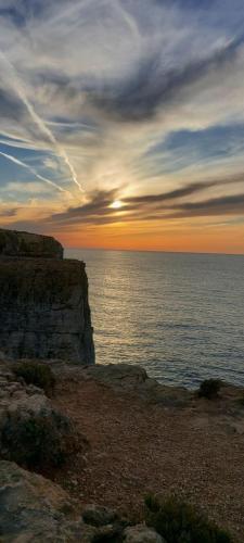 a sunset over the ocean on a rocky cliff at Haven Farmhouse with Private Pool and Sea Views in Għajn Melel