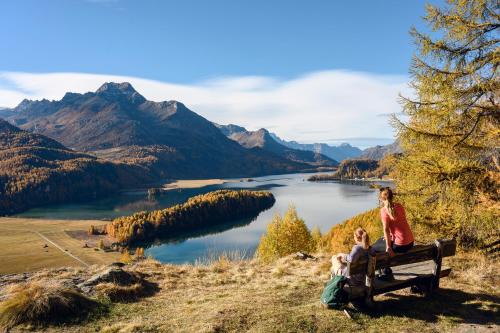 two people sitting on a bench overlooking a lake at Hotel Schweizerhof Sils Maria, a Faern Collection Hotel in Sils Maria