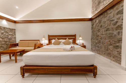 a bedroom with a king sized bed with a stone wall at Le Montfort Resort in Munnar