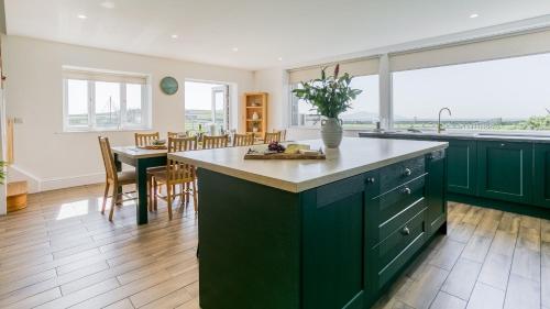 a kitchen with green cabinets and a dining room with a table at Swn y Mor Trefadog in Llanfaethlu