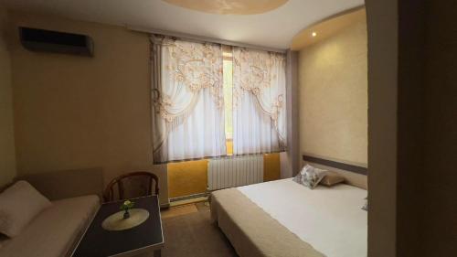 a bedroom with a bed and a table and a window at Семеен Хотел Русалка in Svishtov