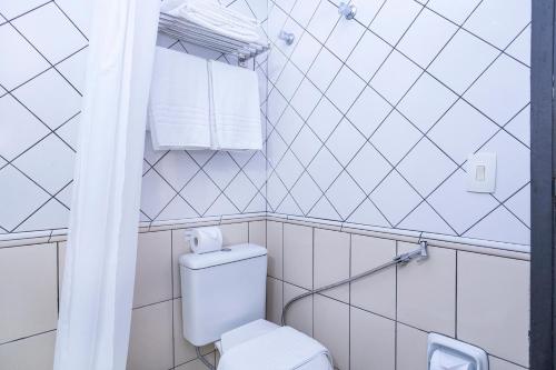 a white tiled bathroom with a toilet and towels at Nikkey Palace Hotel in Sao Paulo