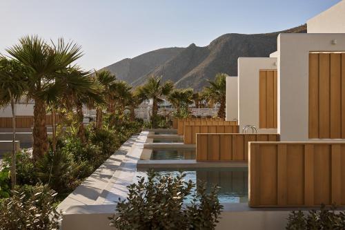 a building with a pool with palm trees and a mountain at Meltemi Blu - Adults Only in Perissa