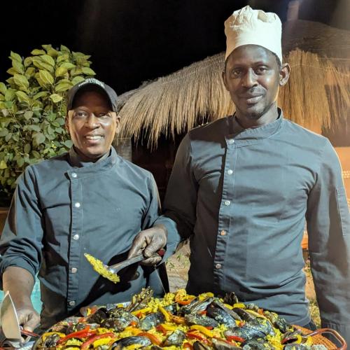 two men standing next to a table of food at LE BENTENIER Home Détente in Nianing
