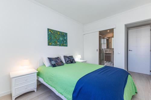 a white bedroom with a green bed and a painting on the wall at Vieira Azul in Armação de Pêra