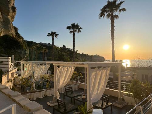 a patio with white curtains and tables and palm trees at H2O TROPEA in Tropea
