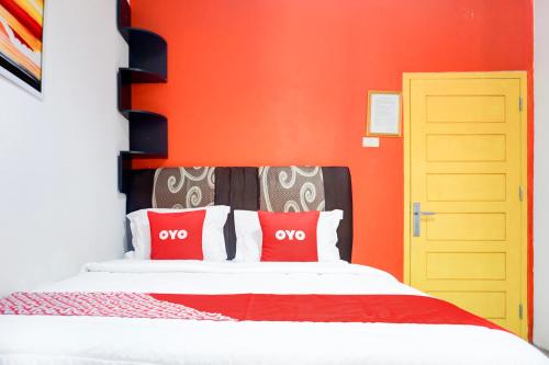 a bedroom with orange walls and a bed with red pillows at Hotel O Bandar Lampung Near Gor Saburai in Bandar Lampung