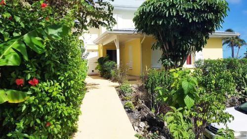 a garden with a yellow house with trees and flowers at La Parenthèse de L'Autre Bord, donnant sur la plage in Le Moule