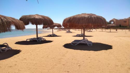 a row of straw umbrellas on a beach at Luxury Chalet in Mountain View 2 , El-Sokhna with Sea View , Pool View and Garden View Families Only in Ain Sokhna