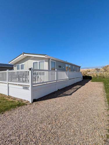 a house with a white fence on a gravel driveway at Dune Haven Luxury Beachside Lodge in Lossiemouth