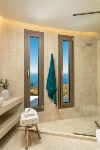 a bathroom with a shower and two windows and the ocean at Minimalist Mediterranean Blue key Villa with Sea View & Infinity Heated Pool in Agia Pelagia