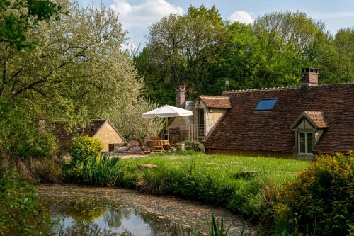 a house with an umbrella next to a pond at Chambres d hôtes du Moulin de Boiscorde in Rémalard en Perche
