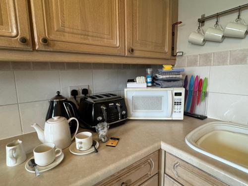 a kitchen counter with a microwave and cups and a sink at Hargate Hall Self Catering in Buxton