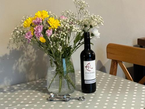a bottle of wine and a vase of flowers on a table at Hargate Hall Self Catering in Buxton