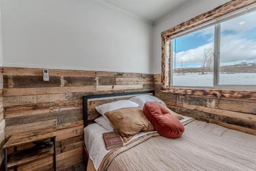 a bedroom with a wooden wall and a bed with a window at Orion Farmstead in Ovando